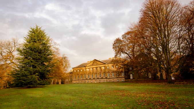 The exterior view of the house at Nostell with grey skies, wintery trees and a grass lawn in front.